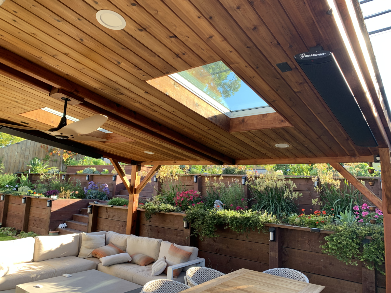 Covered redwood patio pergola with skylight, ceiling fan, heaters, and outdoor seating area.
