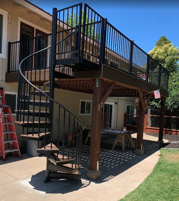 Elevated backyard deck with black metal railing, wood support posts, and spiral stairs.