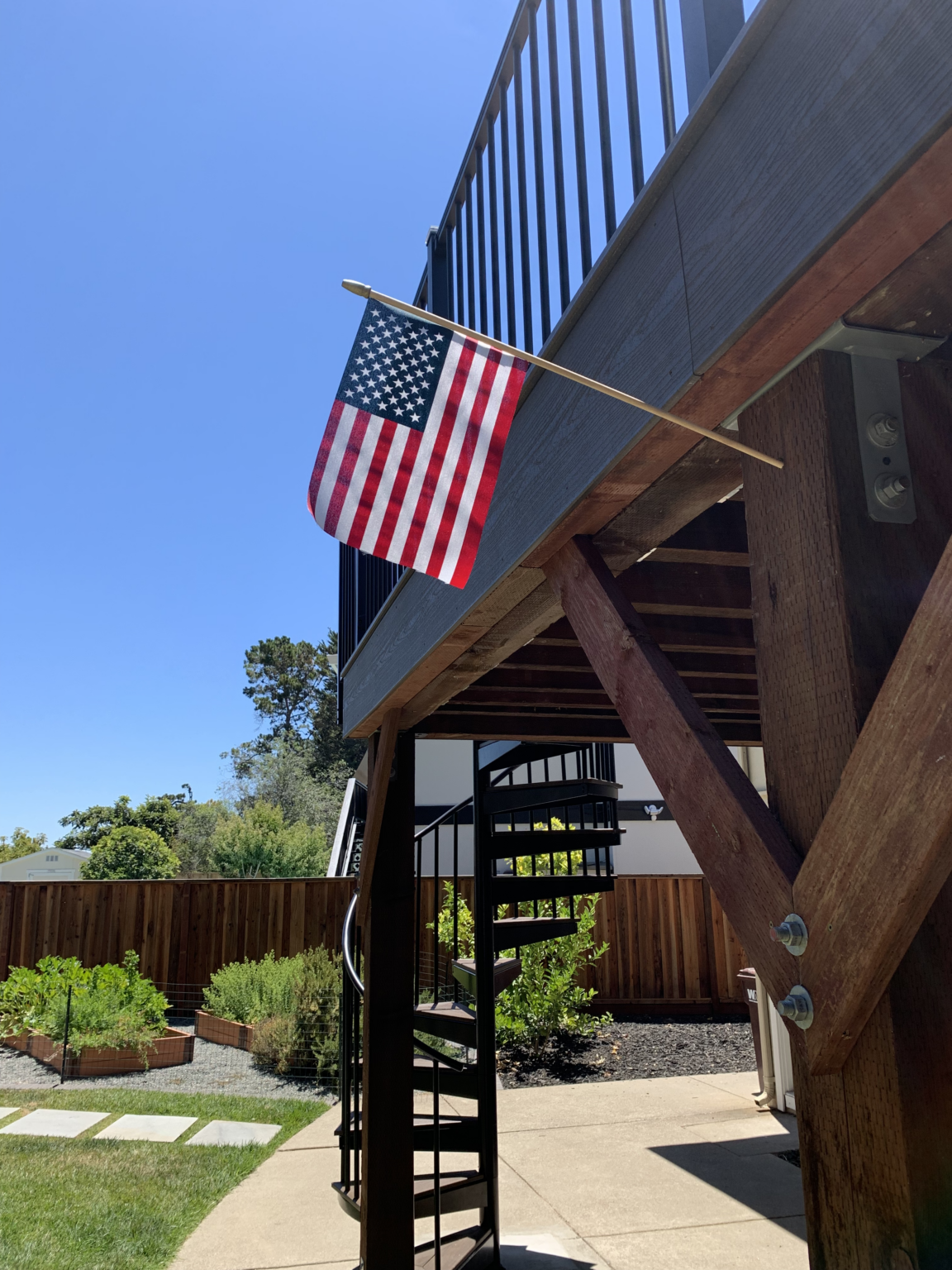 Elevated deck with black railing, spiral stairs, wood framing, and American flag.