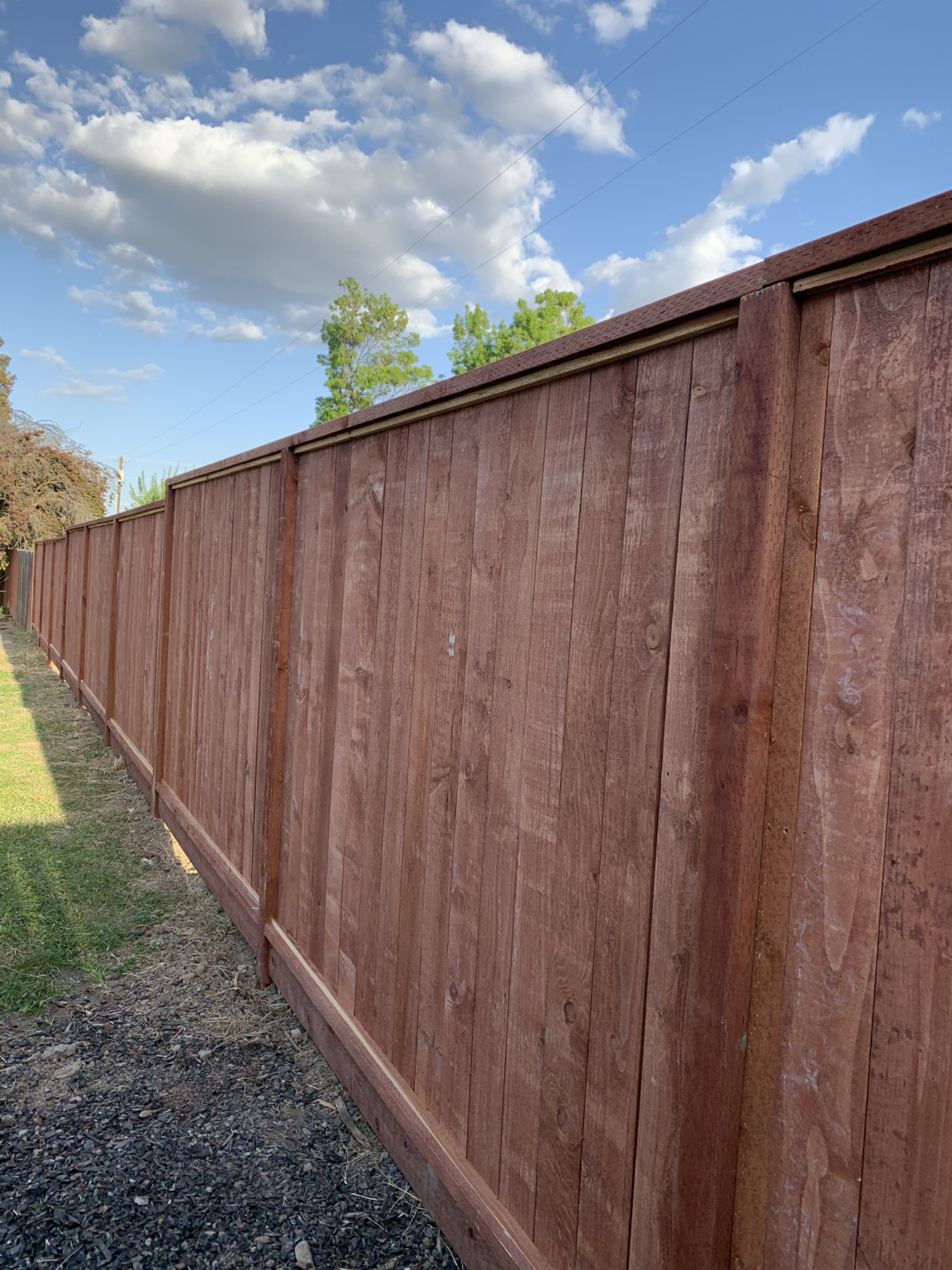 Long redwood privacy fence with framed construction and stained wood boards.