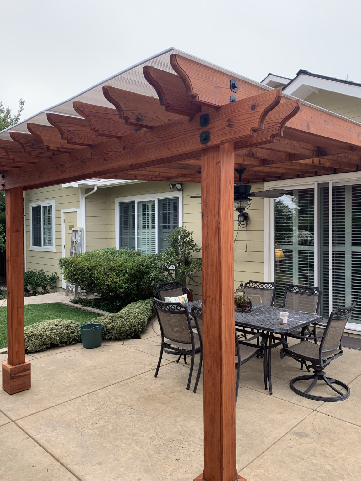 Redwood backyard pergola patio cover with decorative rafter tails and stained wood posts.
