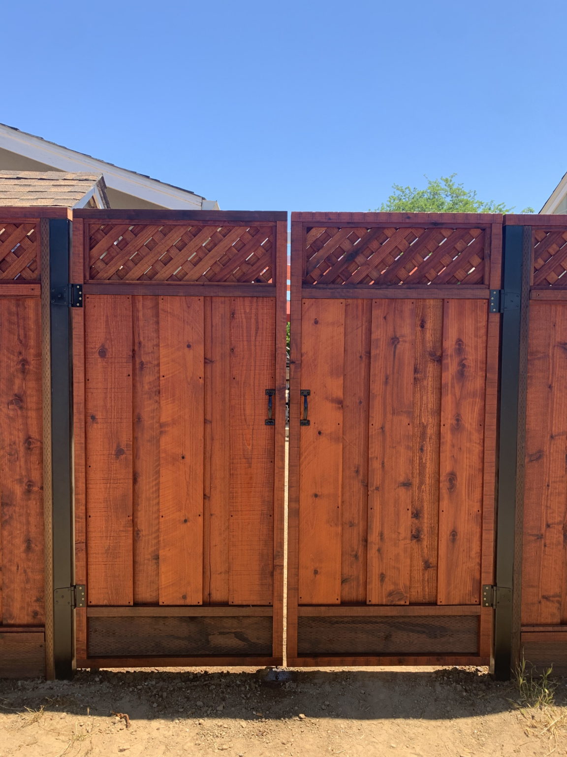 Redwood double gate with lattice top, black steel posts, and black gate hardware.