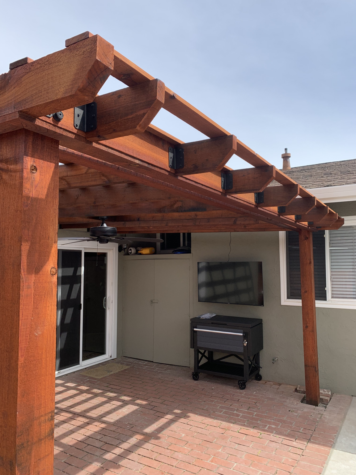 Redwood patio pergola with metal roof over an outdoor bar and seating area.