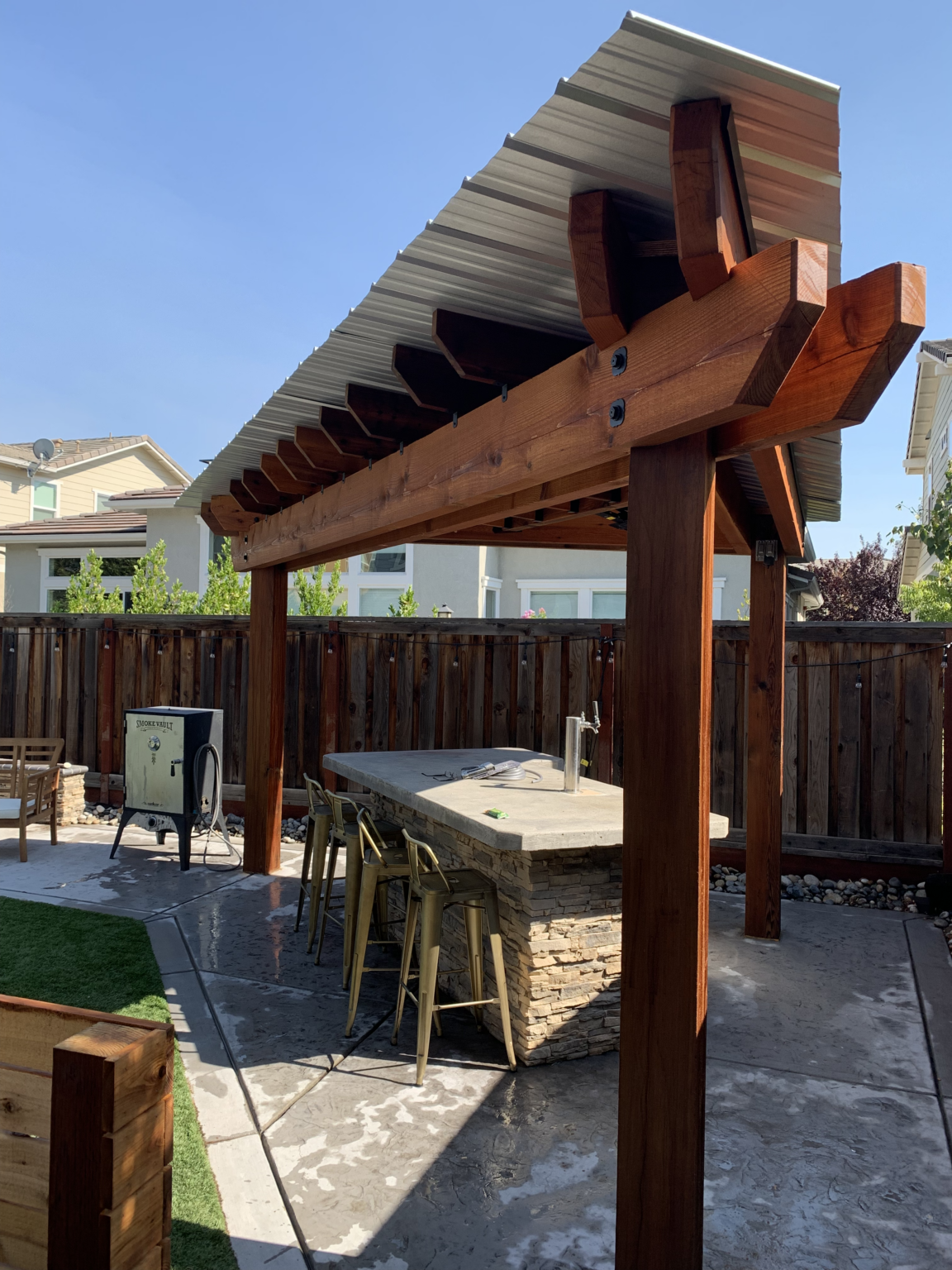 Redwood pergola with metal roof covering an outdoor bar area.
