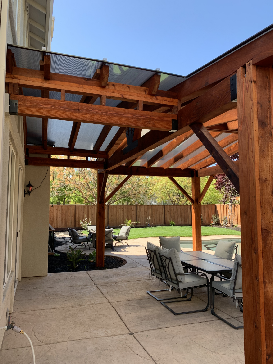 Redwood pergola with polycarbonate roof panels over a backyard patio.