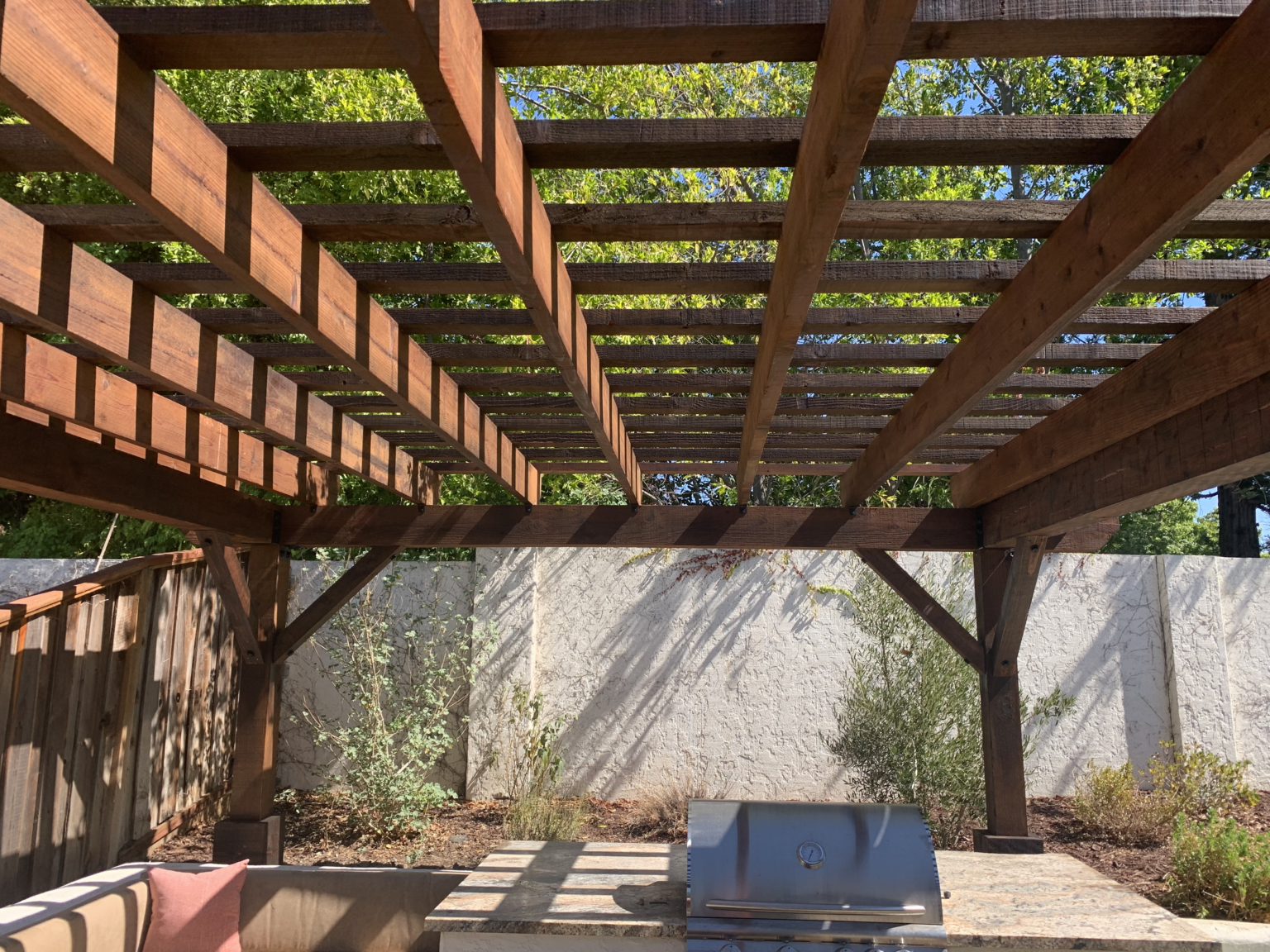 Close-up of redwood pergola rafters above an outdoor kitchen area.