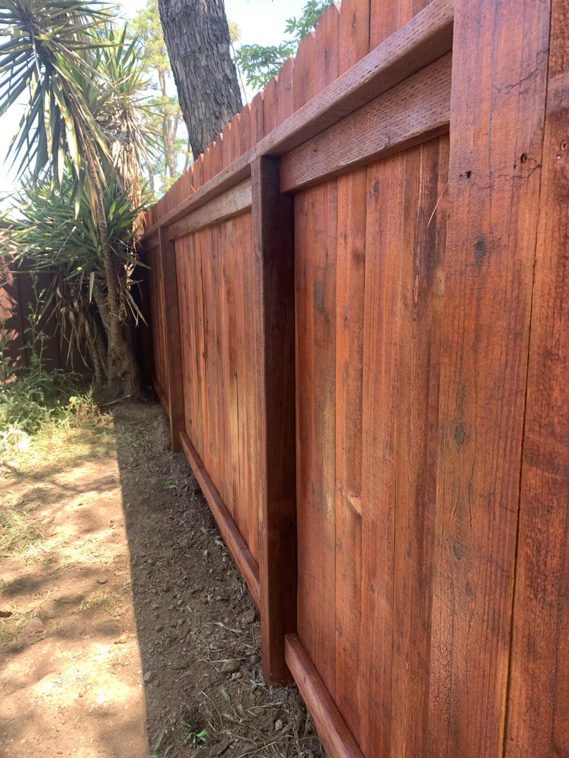 Close-up detail of stained redwood privacy fence with framed rails and vertical boards.
