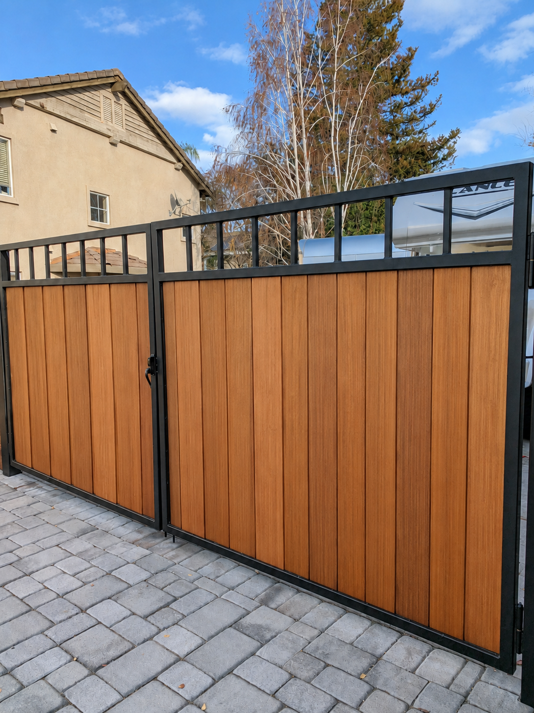 Steel-framed wood driveway gate with black metal frame and vertical wood infill.
