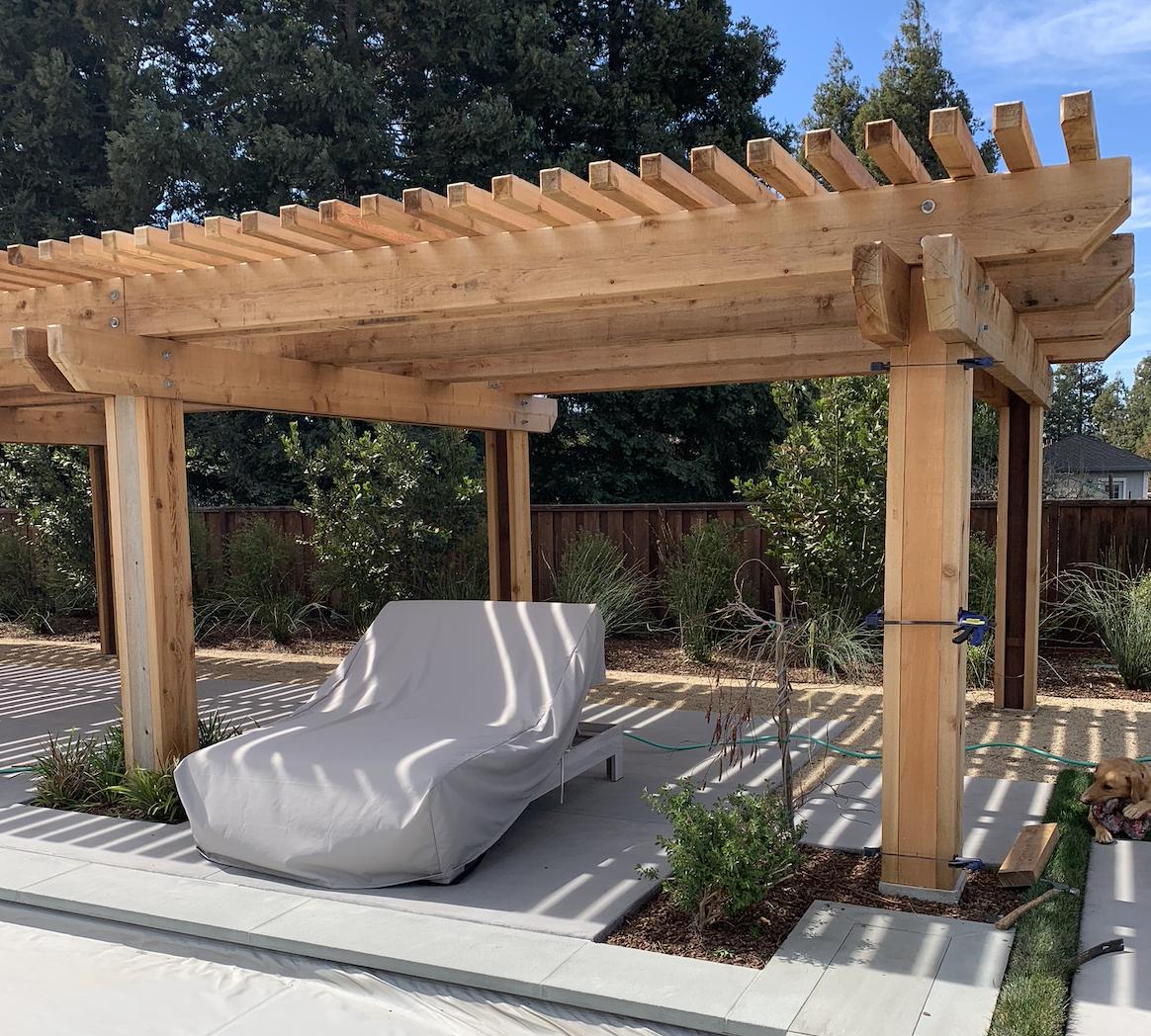 Wood poolside pergola patio cover built next to a backyard pool area.